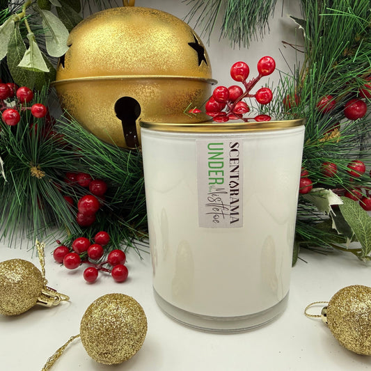 White candle with a gold lid surrounded by Christmas decorations on a white surface
