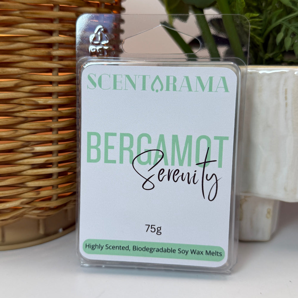 A packaged wax melt product labeled SCENTARAMA BERGAMOT Serenity, 75g, standing upright on a white surface with a wicker wax warmer and potted plants in the background.