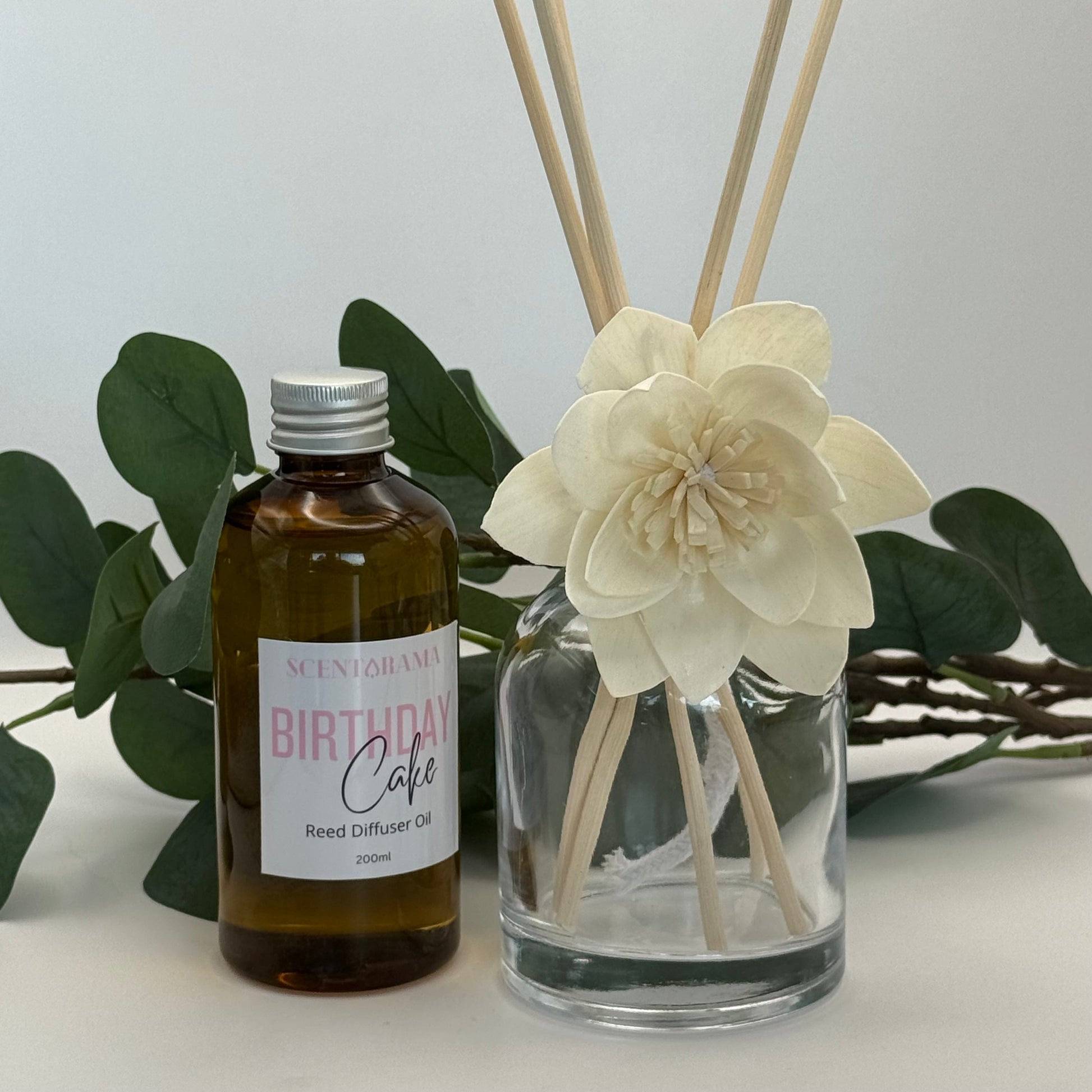 Reed diffuser set with bottle labeled 'Birthday Cake' and decorative flower on a light background