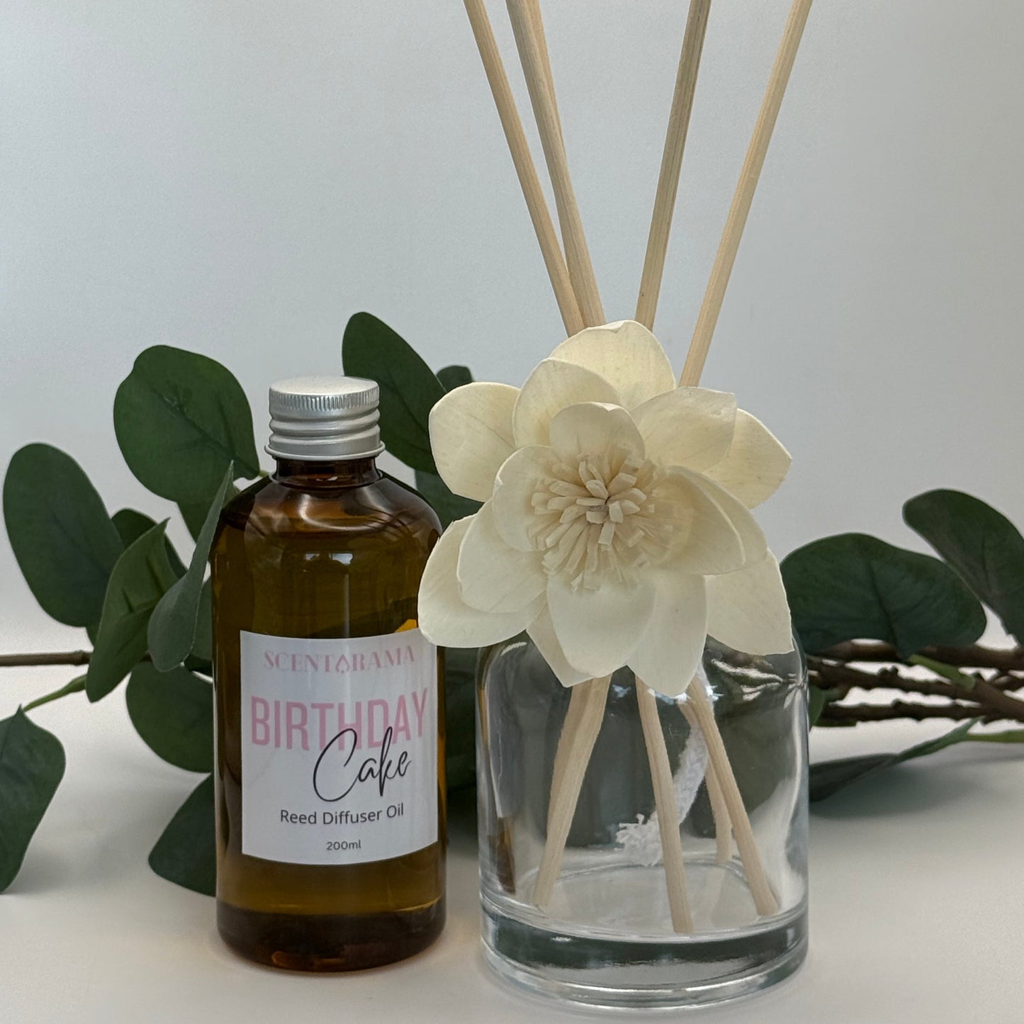 Diffuser with floral design and 'Birthday Cake' bottle on a white background