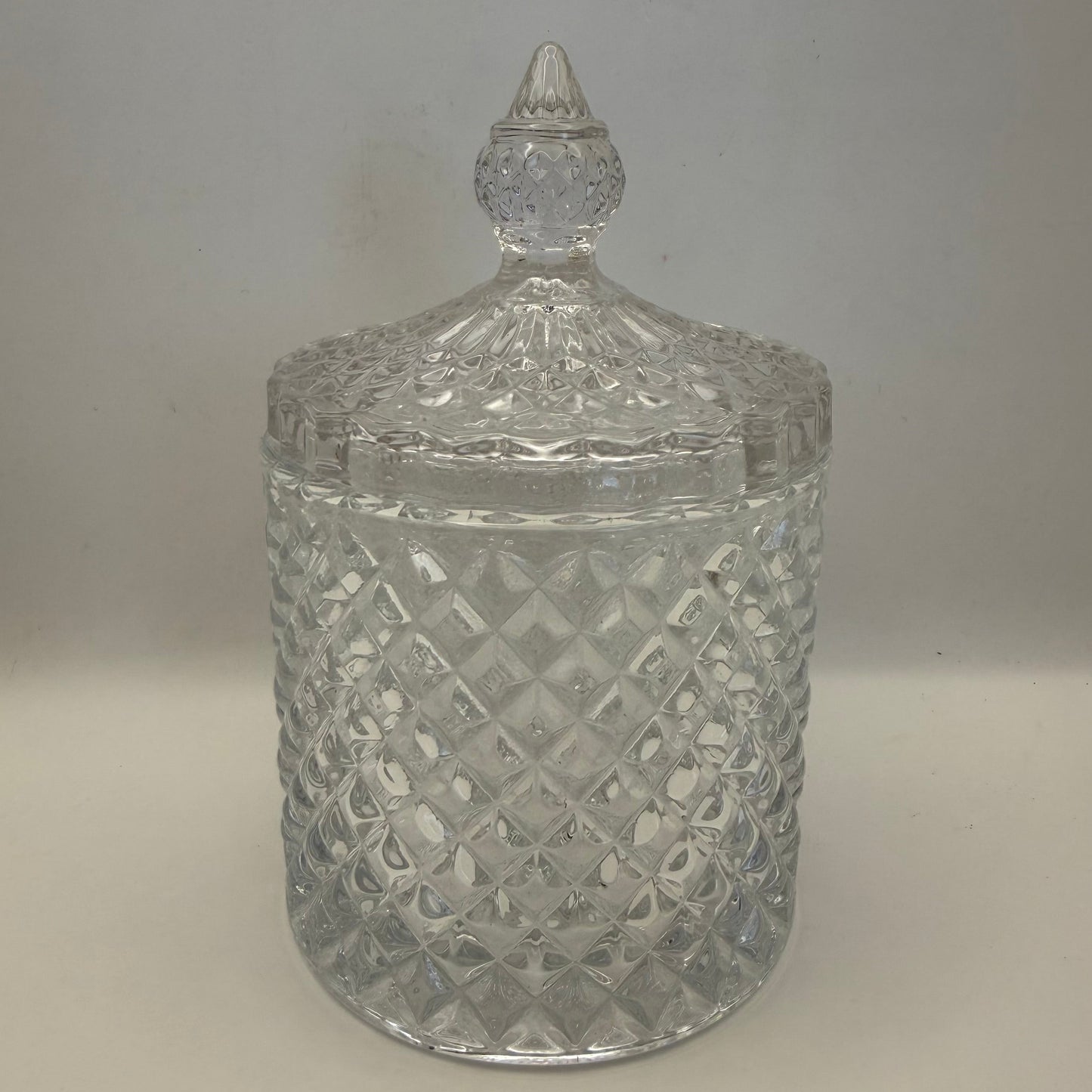 Clear glass candle jar with diamond pattern and textured lid on a plain background