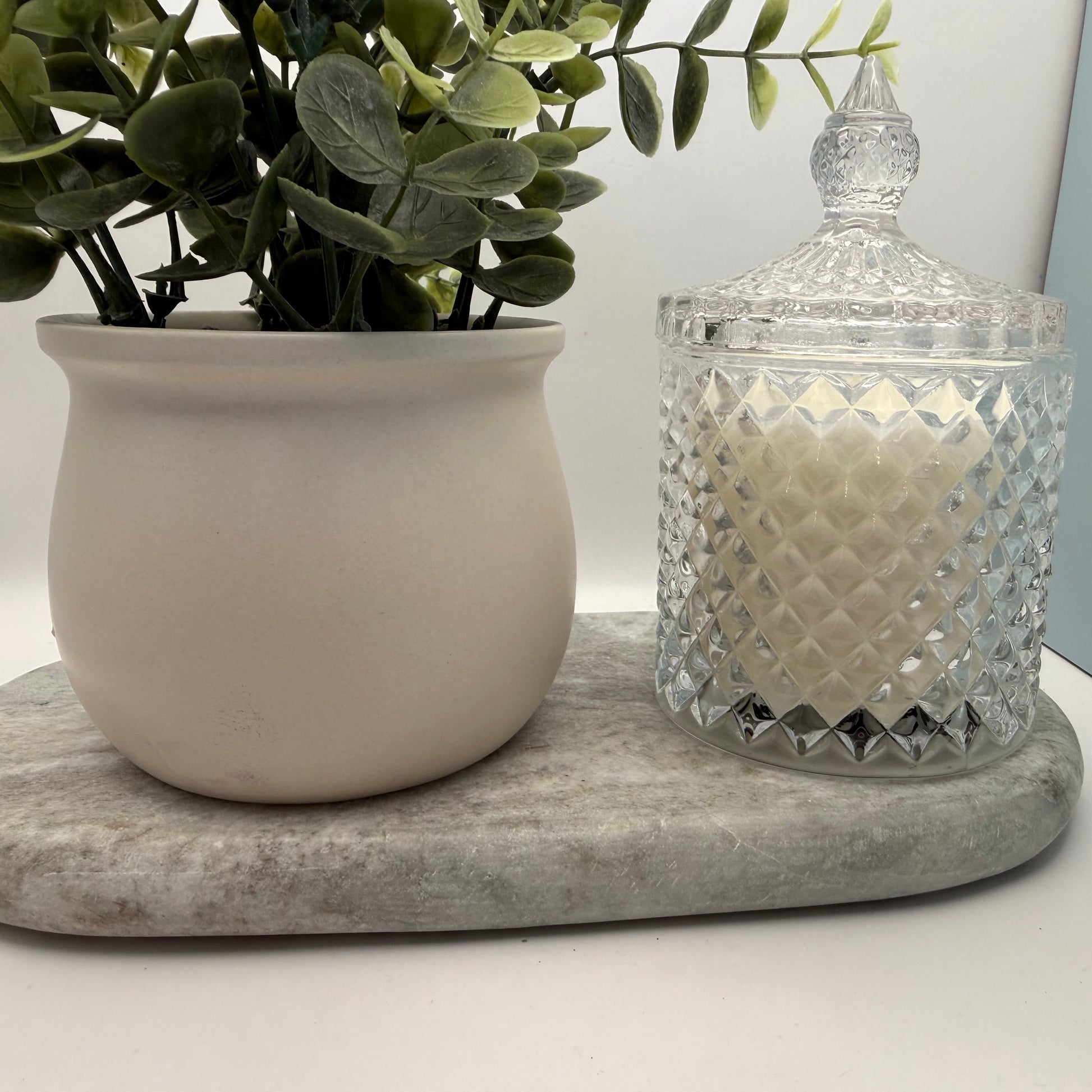 Decorative glass jar with a candle and a potted plant on a marble coaster.