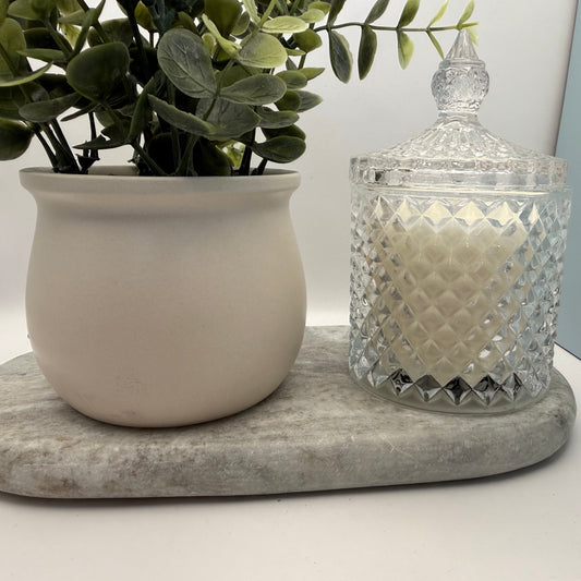 Decorative glass jar with a candle and a potted plant on a marble coaster.
