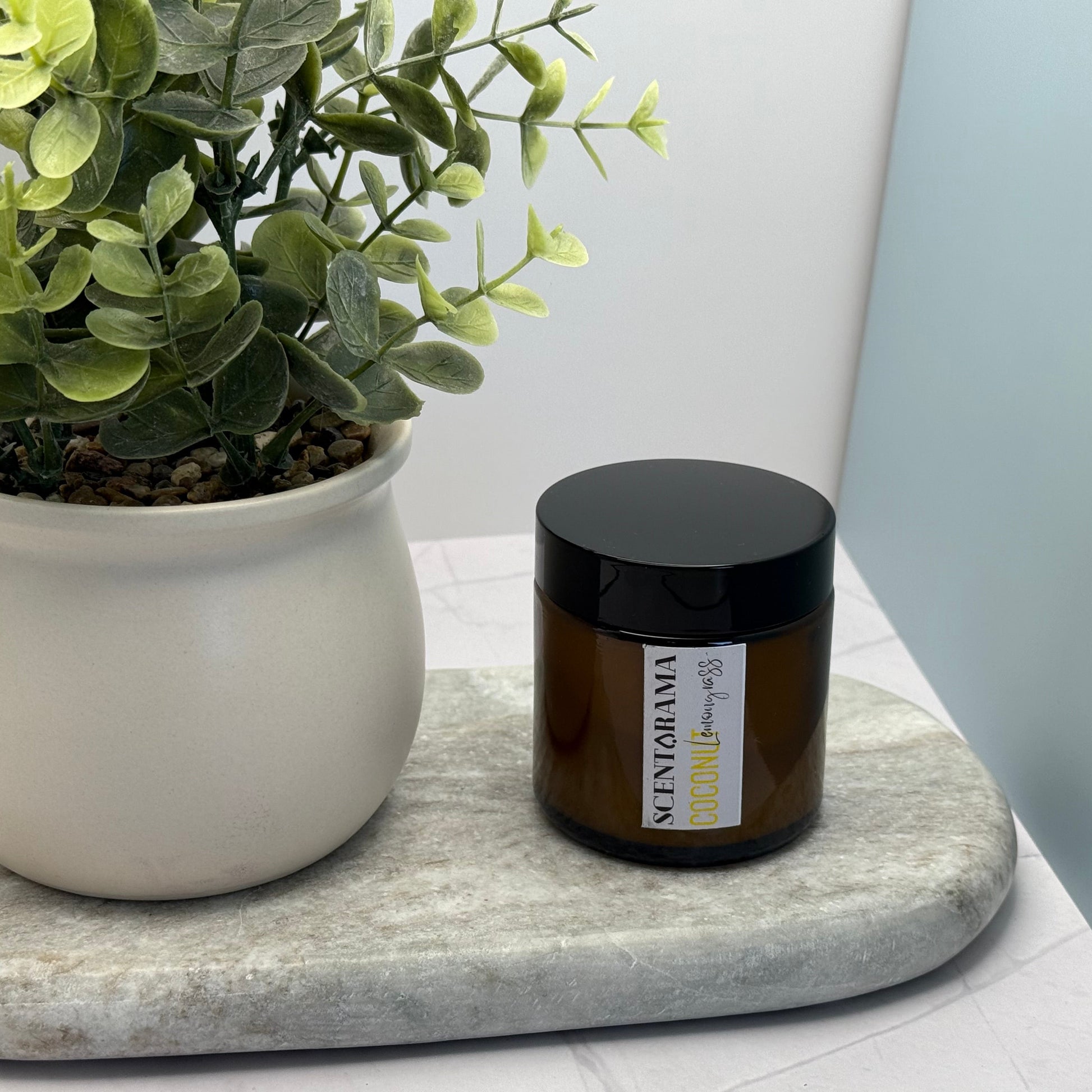 Small Amber Candle Jar in Coconut Lemongrass scent featuring a Scentarama Label on a marble tray next to a pot plant