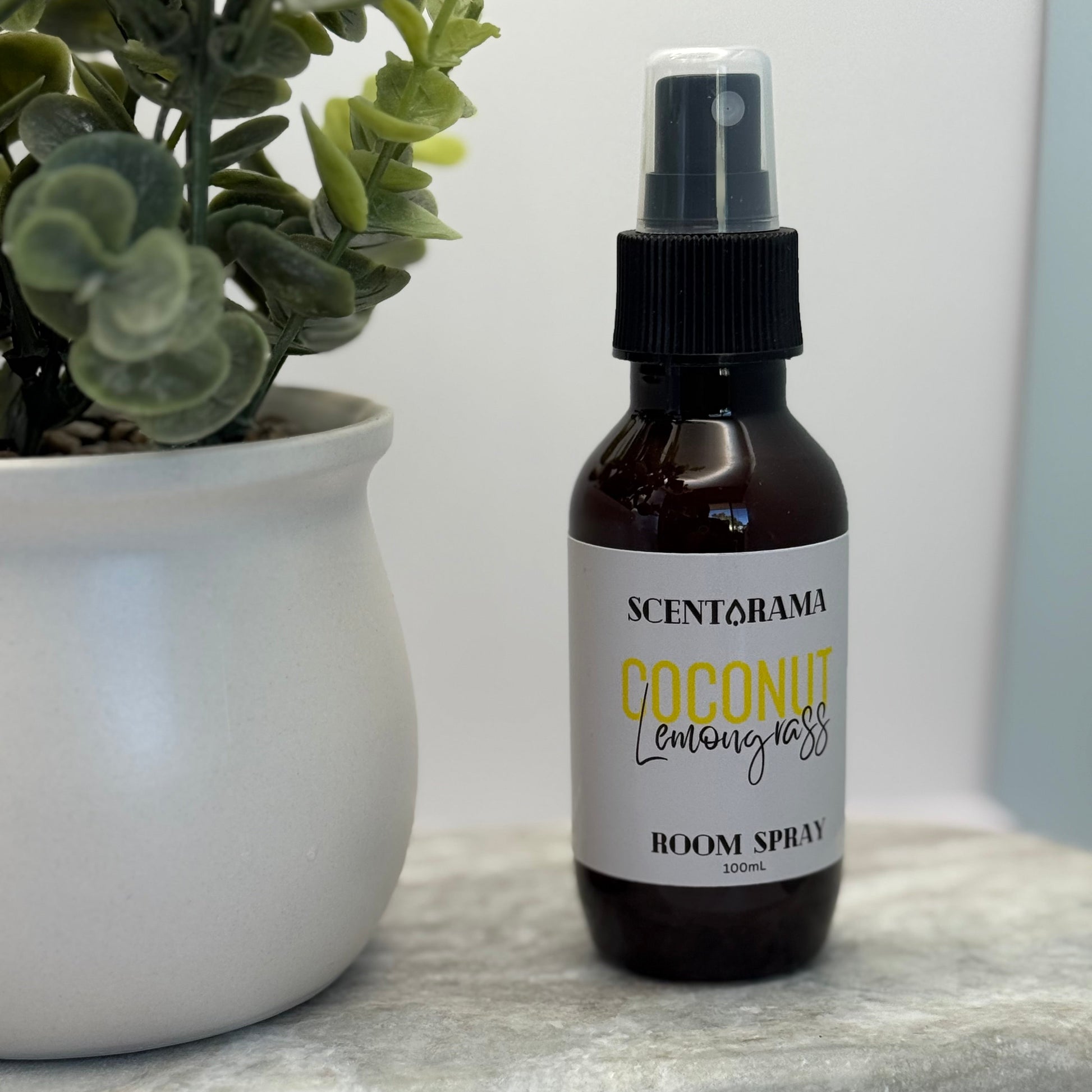 Bottle of Scentarama coconut lemon grass room spray on a marble surface with a plant in the background.
