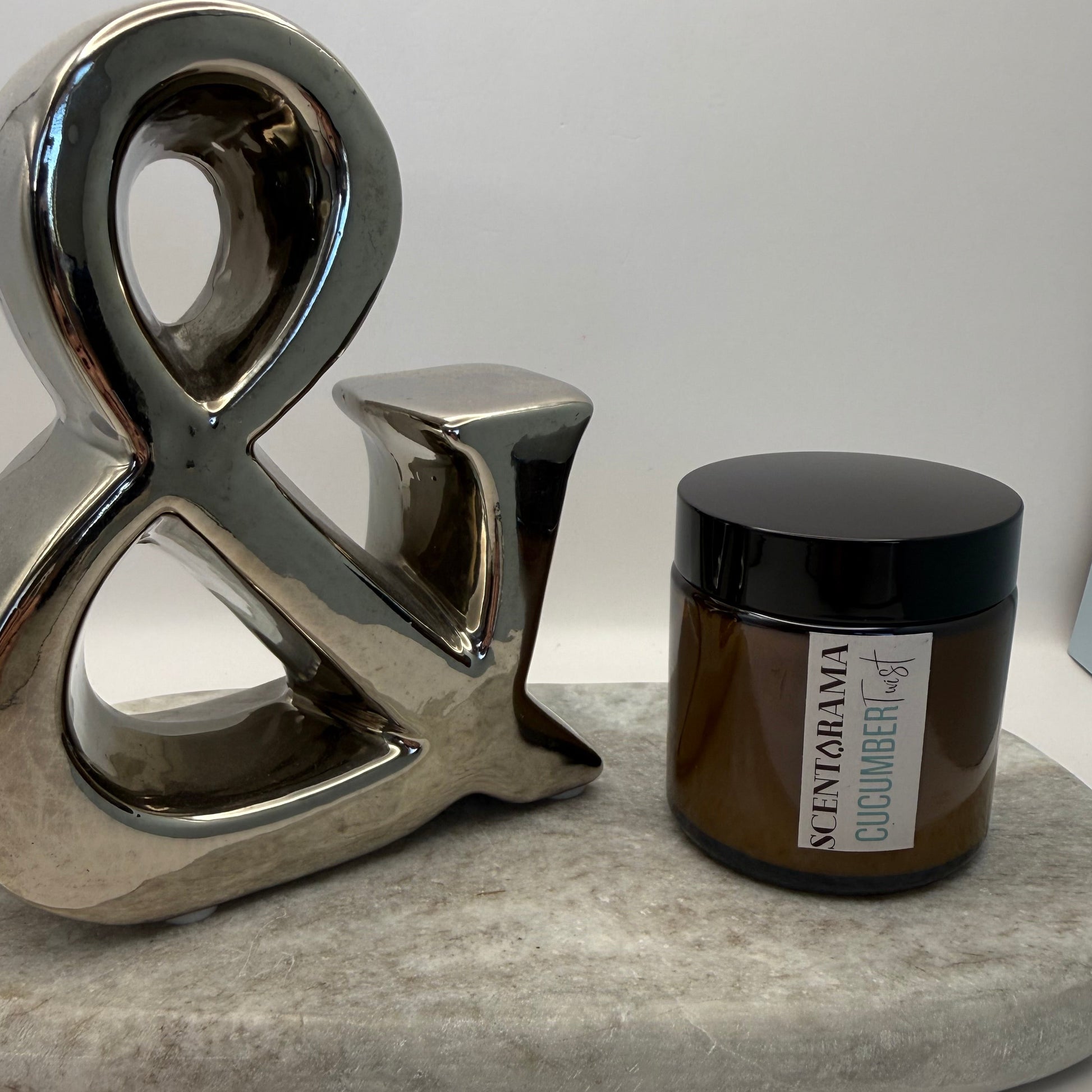 Chrome Ambersand decor with a small amber cucumber twist candle featuring a Scentarama label on a marble tray