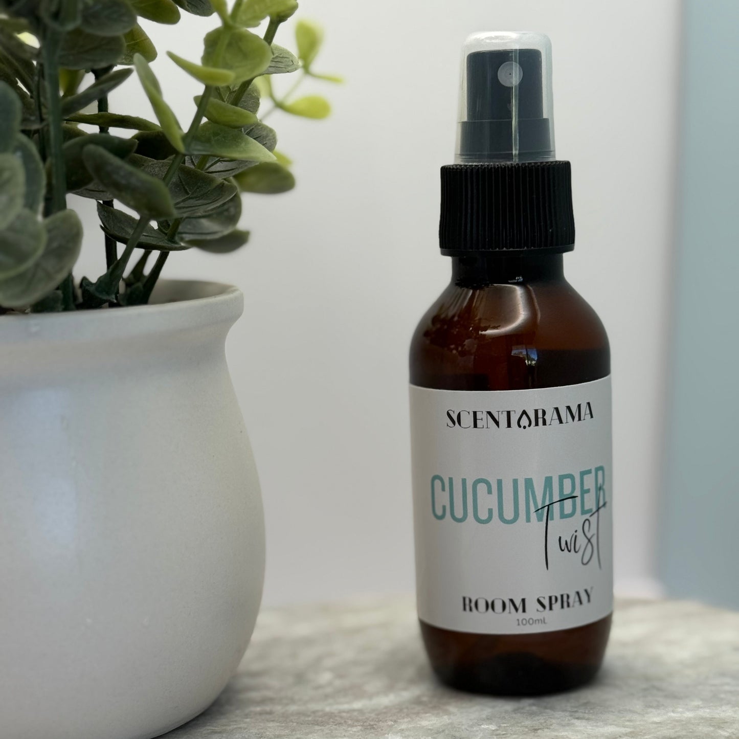 Bottle of Scentorama Cucumber Twist room spray next to a potted plant on a marble surface.