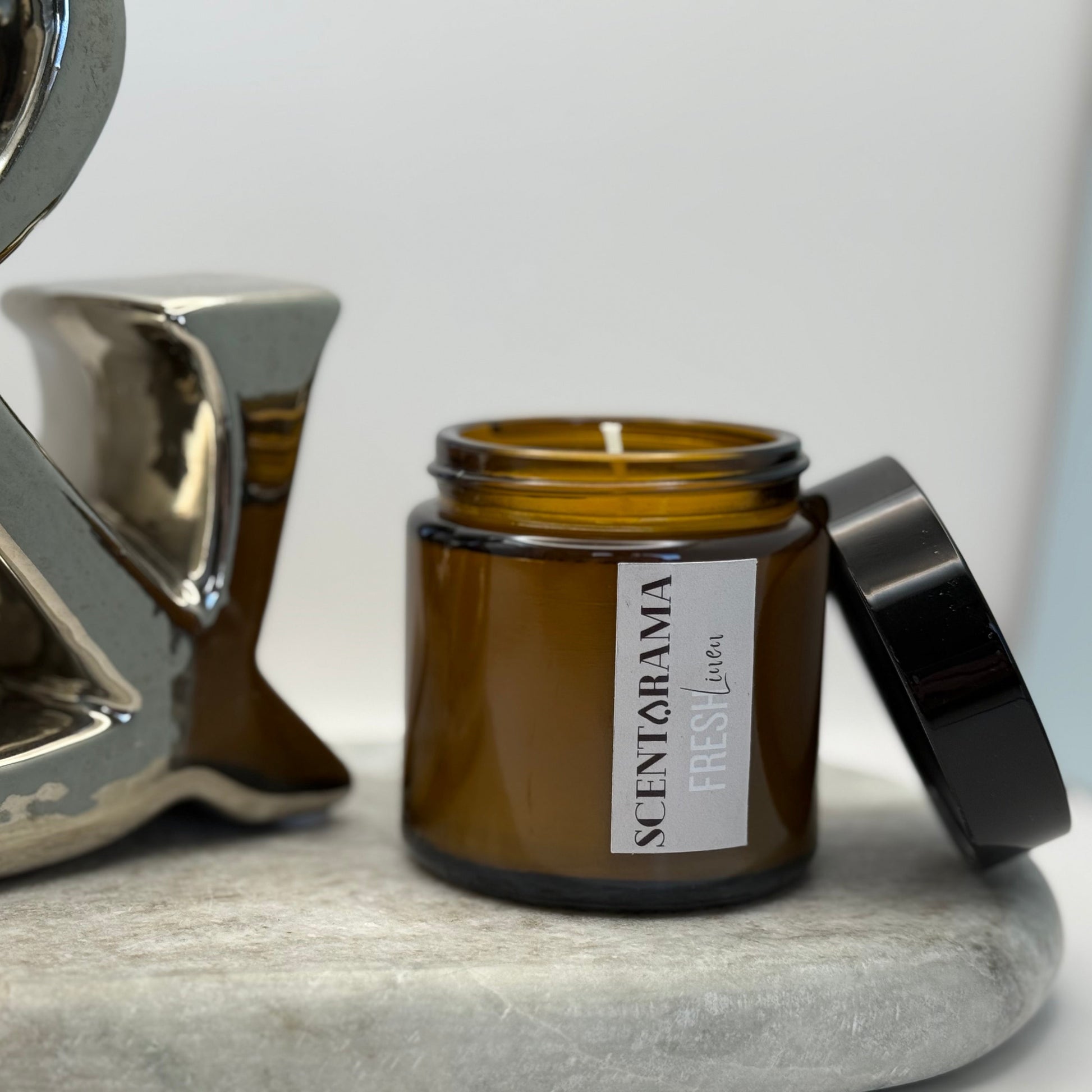 Amber candle jar in Fresh Linen Scent with black lid on a white surface, featuring 'Scentarama' branding.