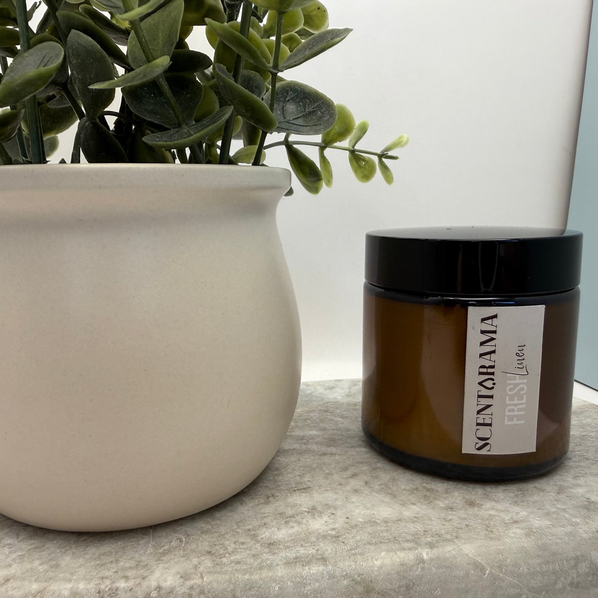 Potted plant and Scentarama Amber jar in Fresh Linen scent on a surface with a neutral background