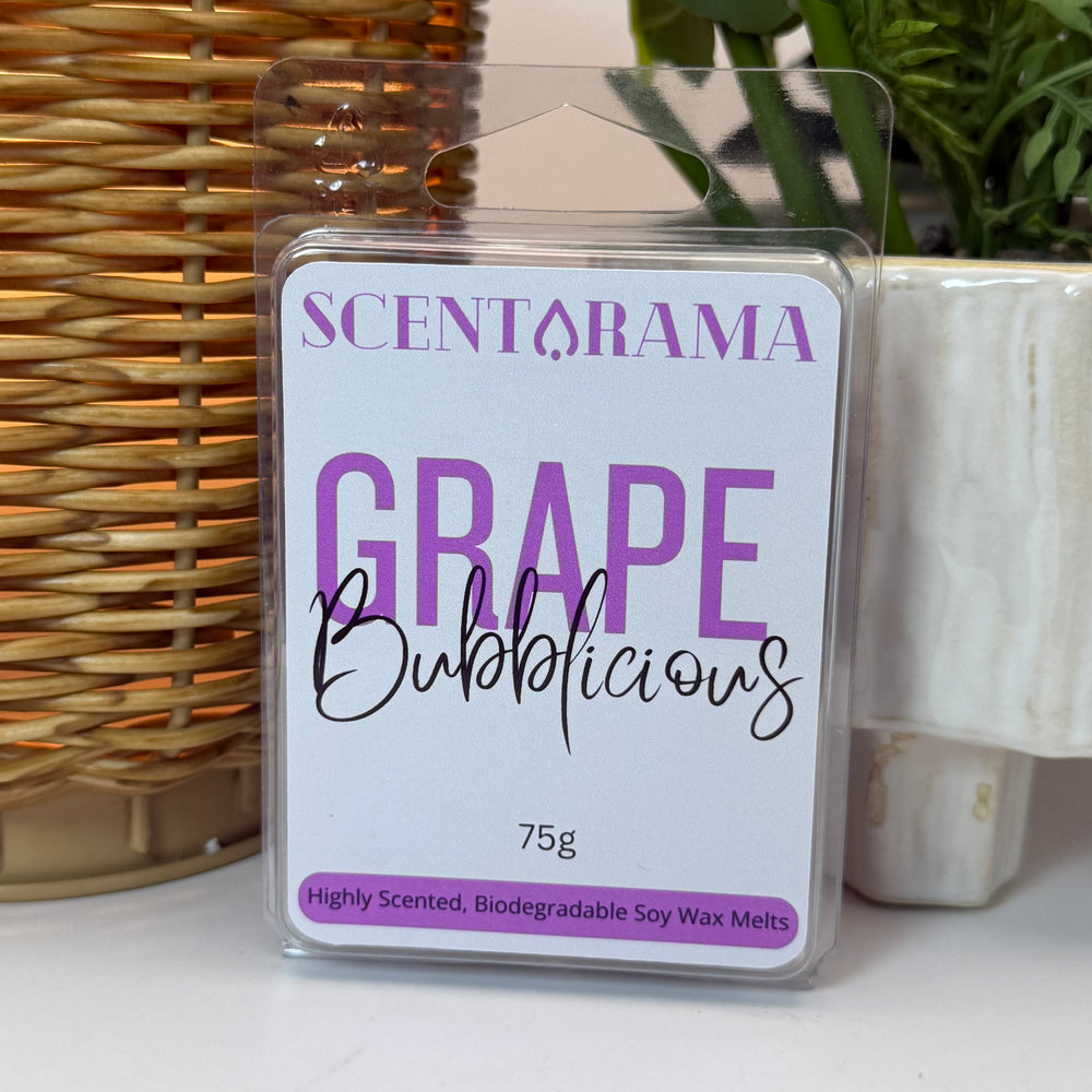 A package of Scentarama Grape Bubblicious soy wax melts, shown in a clear plastic clamshell pack with a white and purple label, set against a background of a wicker wax melt warmer and a potted plant.