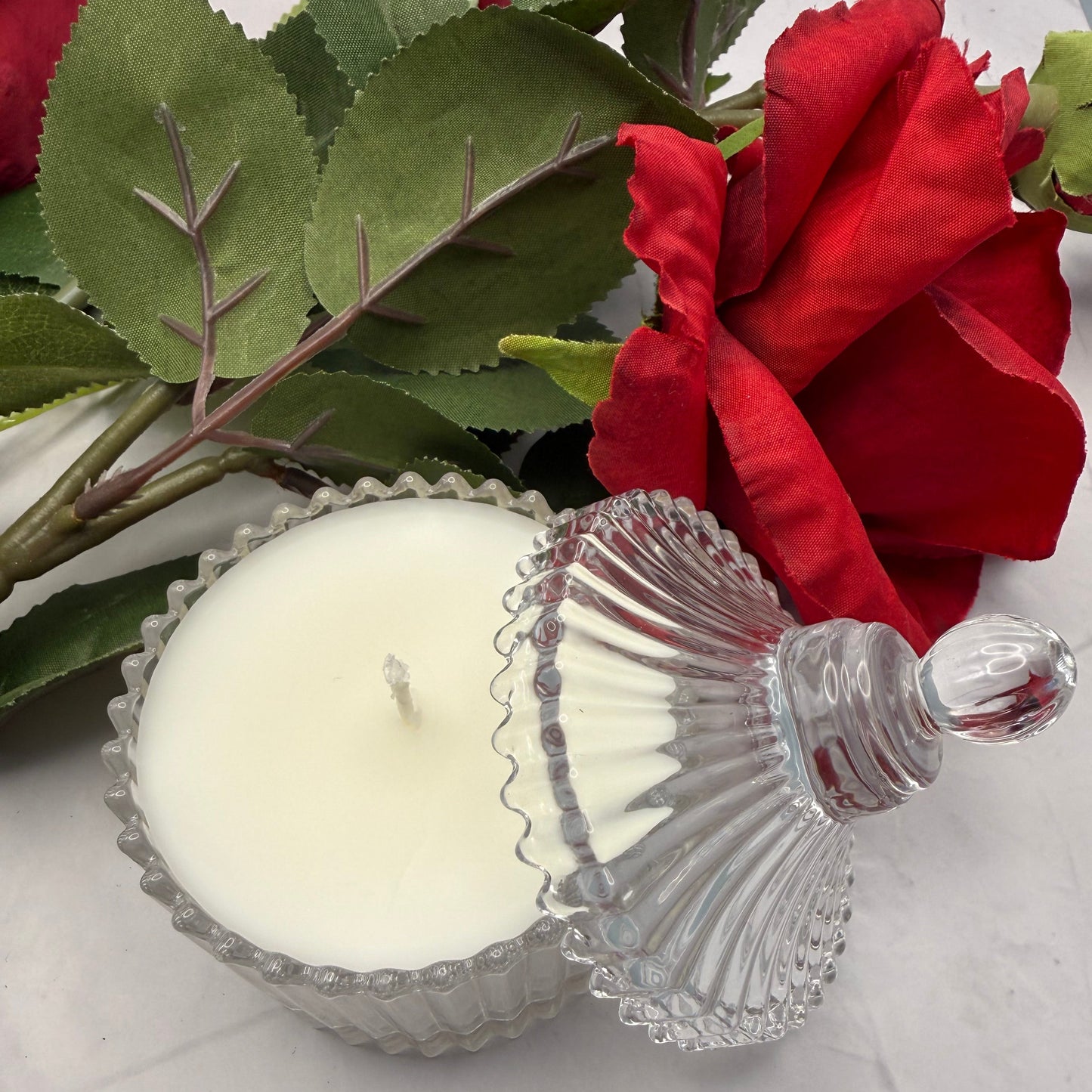 Decorative scentarama candle in a glass holder with a red rose on a light gray background