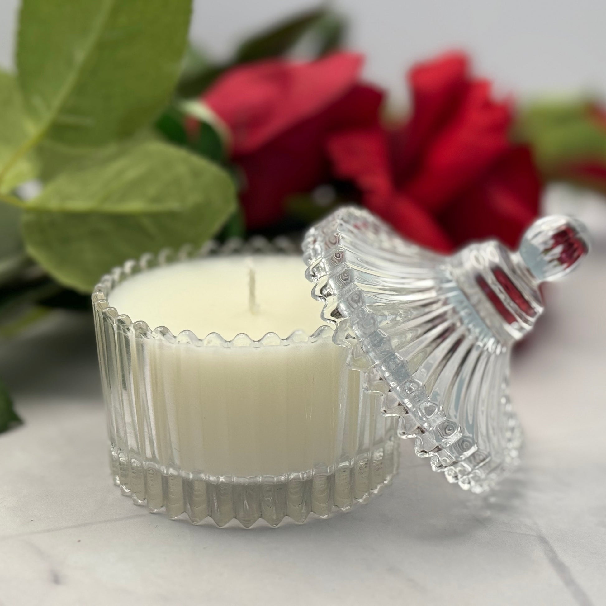 Scentarama Candle in a decorative glass holder with red roses and green leaves in the background
