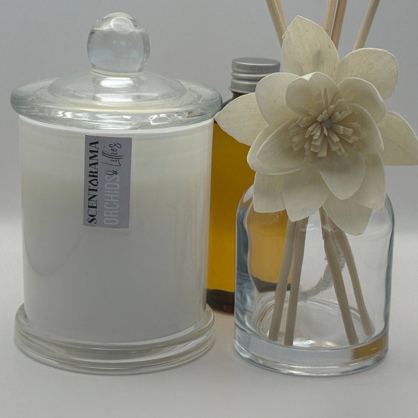 A glass candle jar and a diffuser with flowers on a light gray background