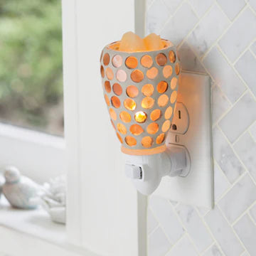 A pearl glass plugable warmer with pearlescent glass circles glowing warm, plugged into a wall socket. Candle Warmers Australia