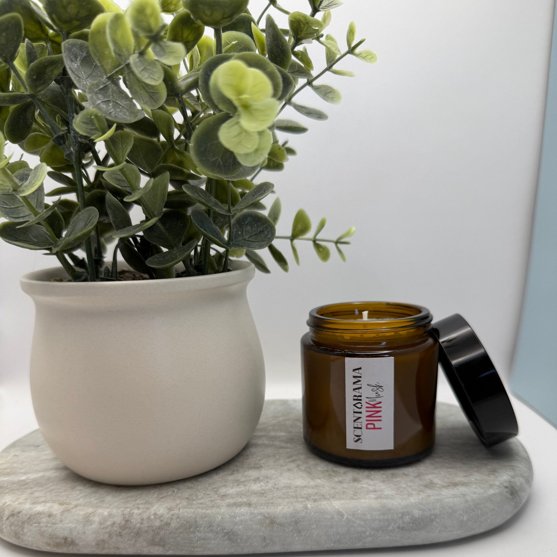 Small amber candle jar in Pink Musk scent with a label on a white surface next to a plant