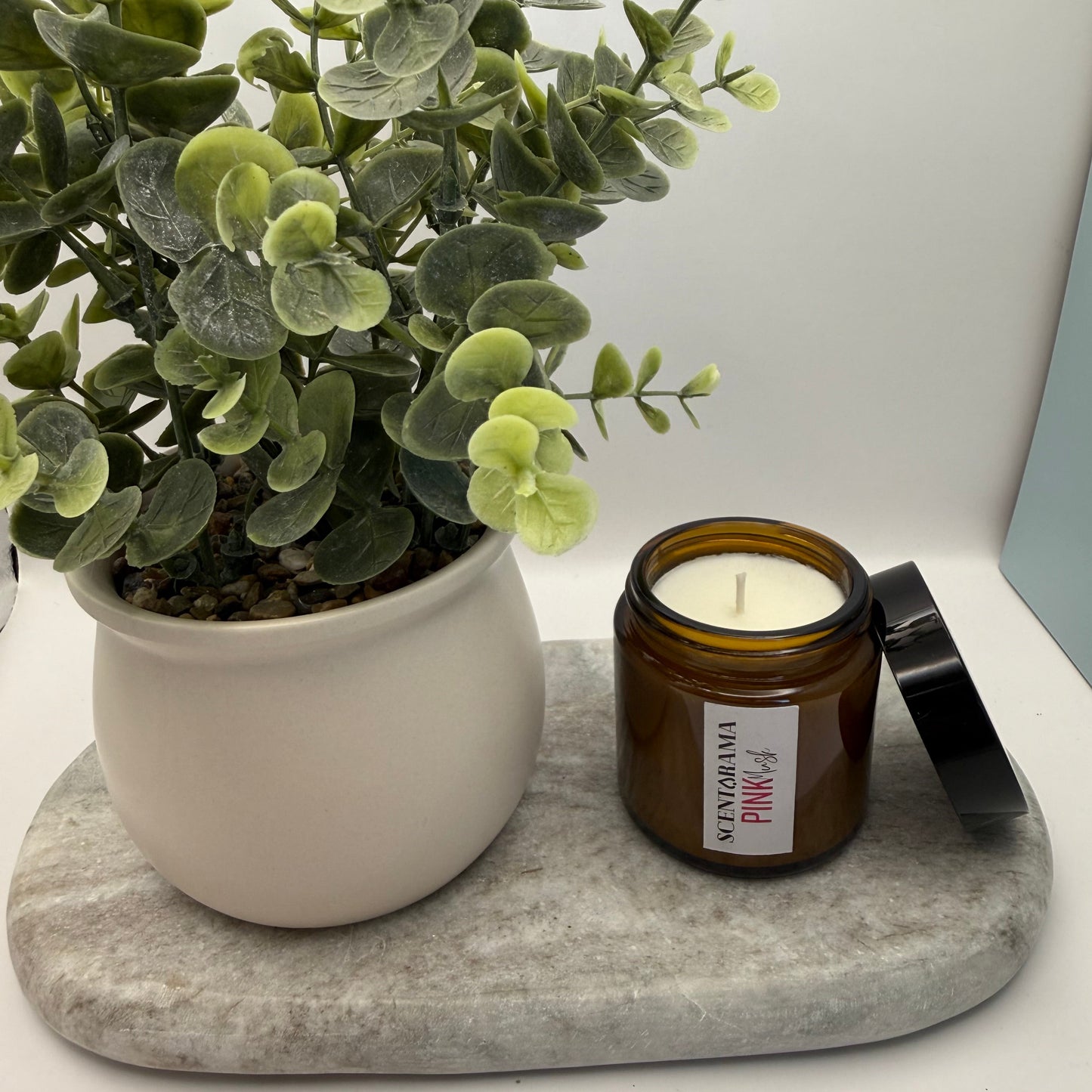 Amber Jar Mini Candle Pink Musk Scent next to a potted plant