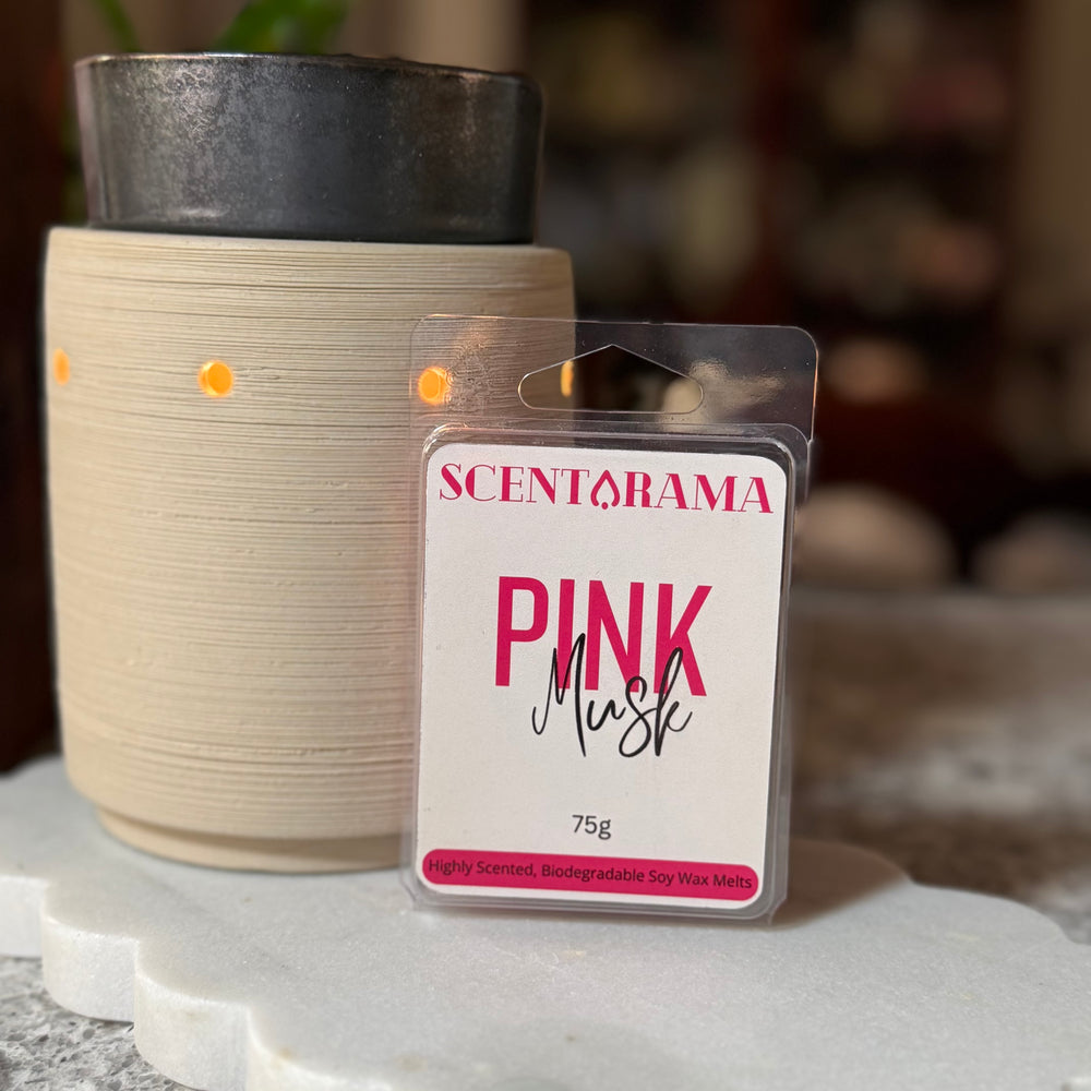 A Scentarama Pink Musk scented wax melt in its clear plastic packaging, displayed in front of a lit cream-colored ceramic wax warmer on a white marble tray.