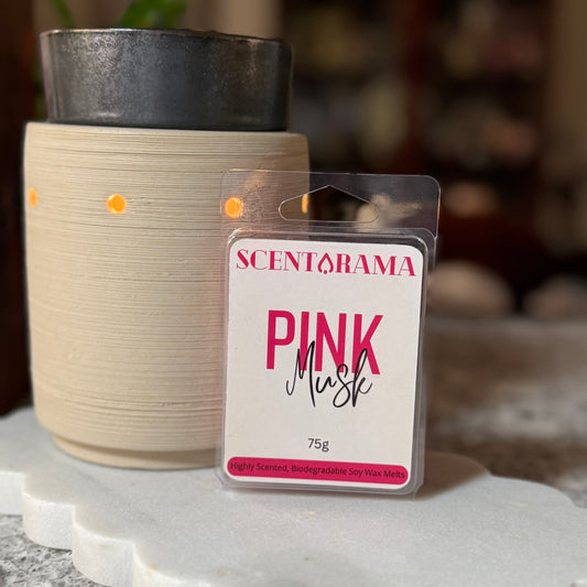 A Scentarama Pink Musk scented wax melt in its clear plastic packaging, displayed in front of a lit cream-colored ceramic wax warmer on a white marble tray.