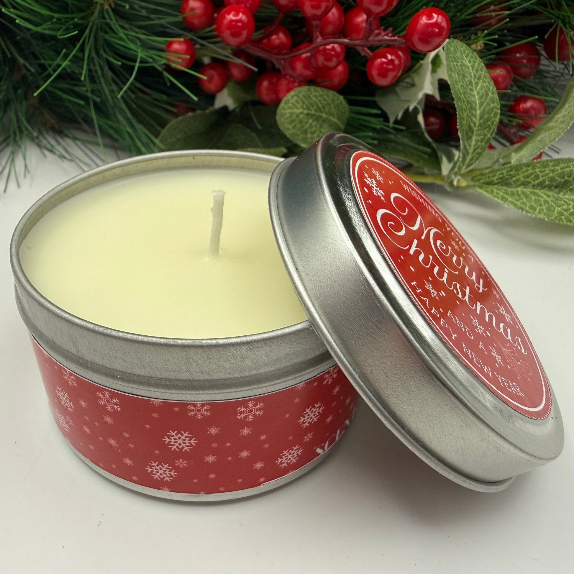 Christmas-themed candle in a tin with holly berries in the background