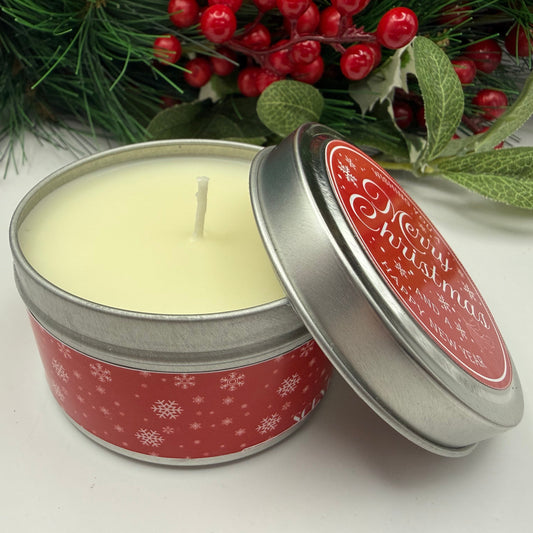 Christmas-themed candle in a tin with holly berries in the background