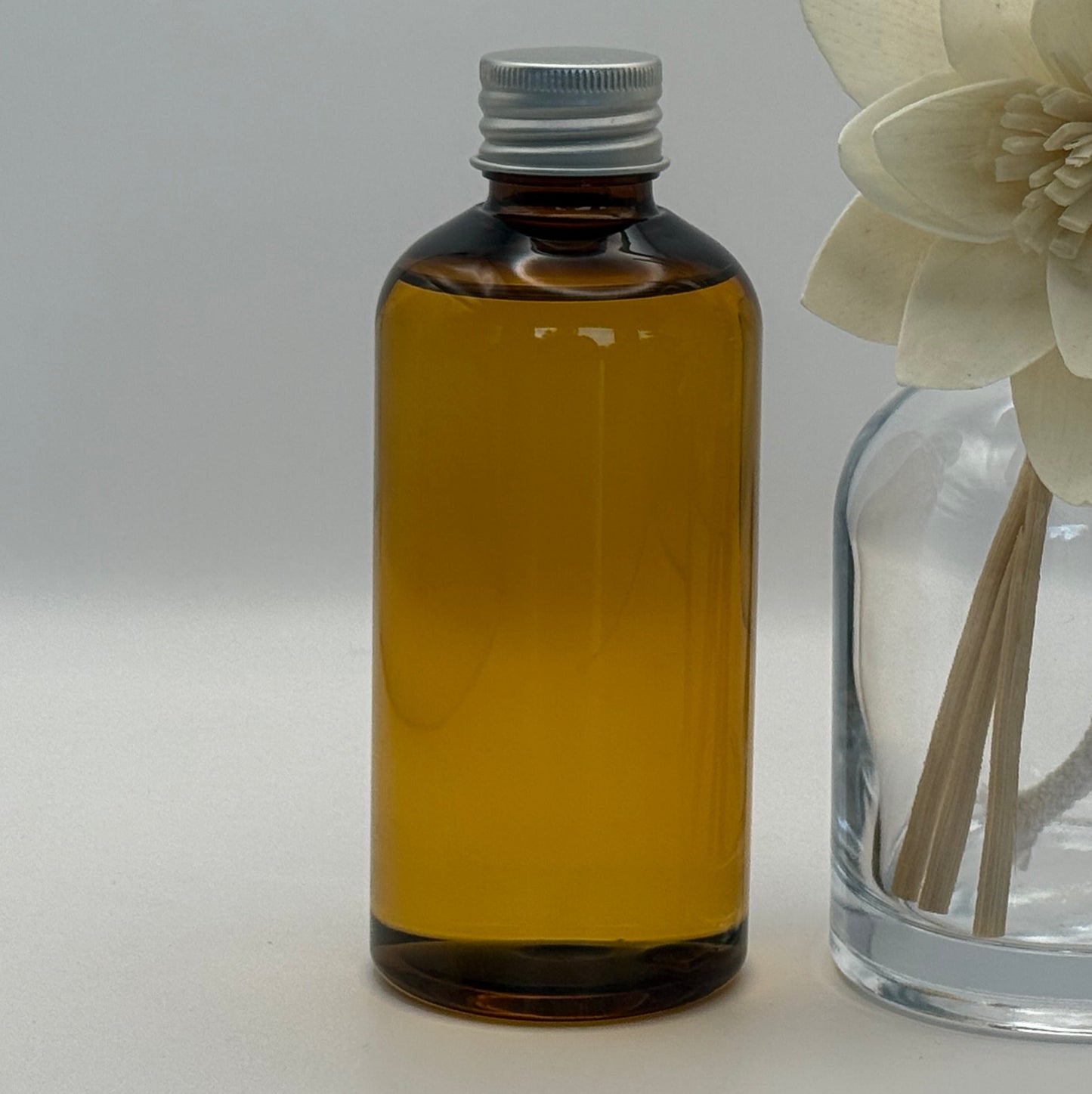 Brown bottle and clear glass diffuser with floral elements on a light gray background