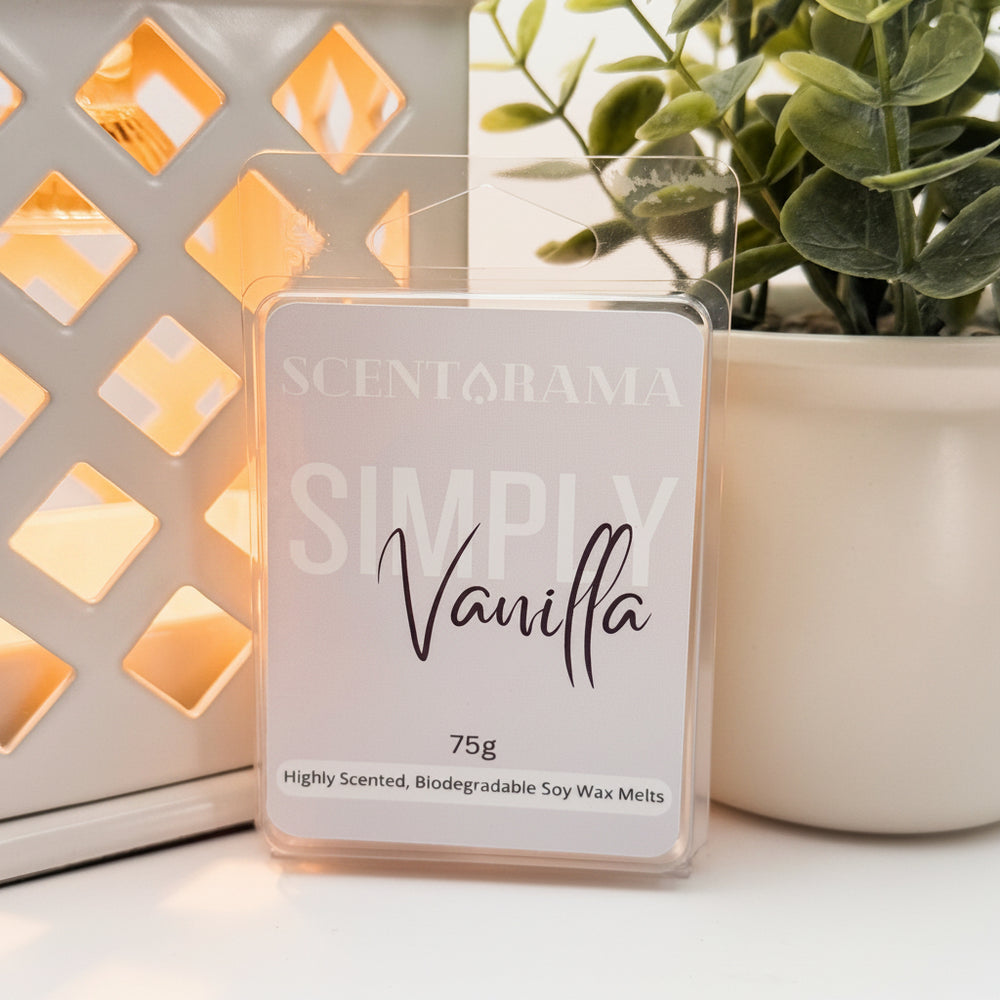 A Scentarama Simply Vanilla 75g scented wax melt in a clear plastic clamshell package, displayed on a white surface next to a lit decorative lantern and a potted plant.