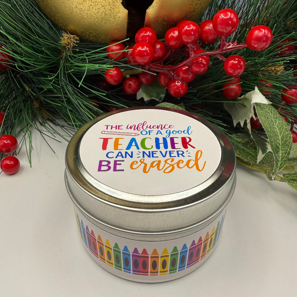 Decorative candle tin with colorful text, gold bell, and greenery on a white background