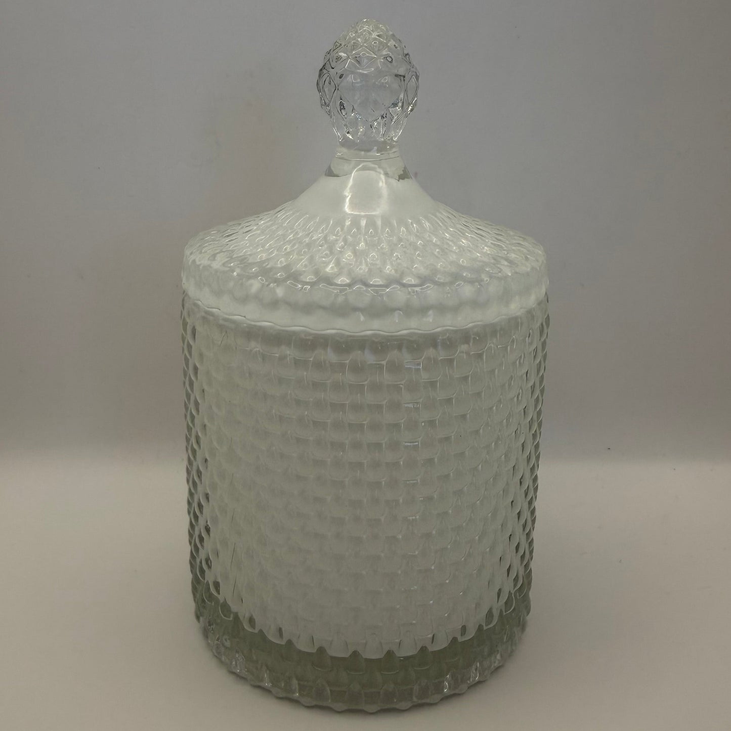 White glass candle jar with textured surface and clear lid on a plain background