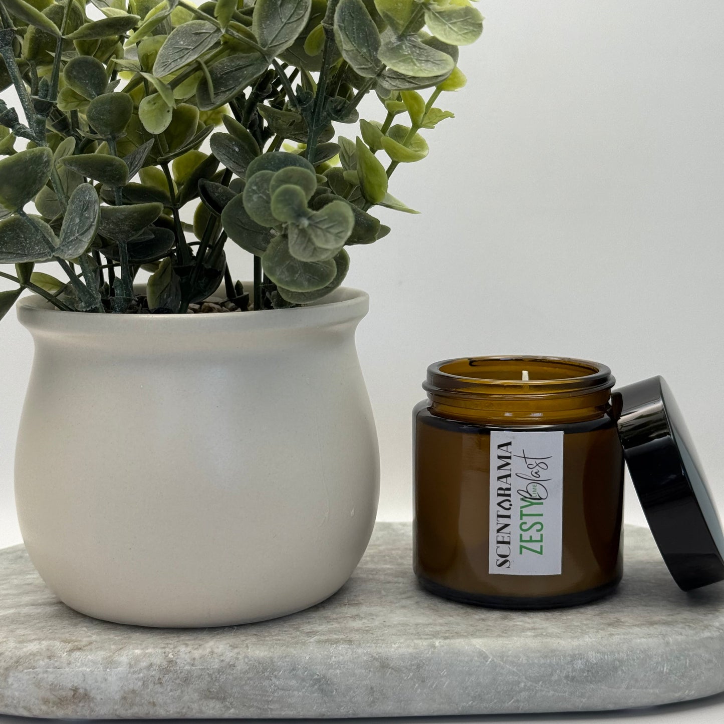 Small Amber candle in Zesty Lime Blast Fragrance featuring a Scentarama label on a white surface next to a green plant