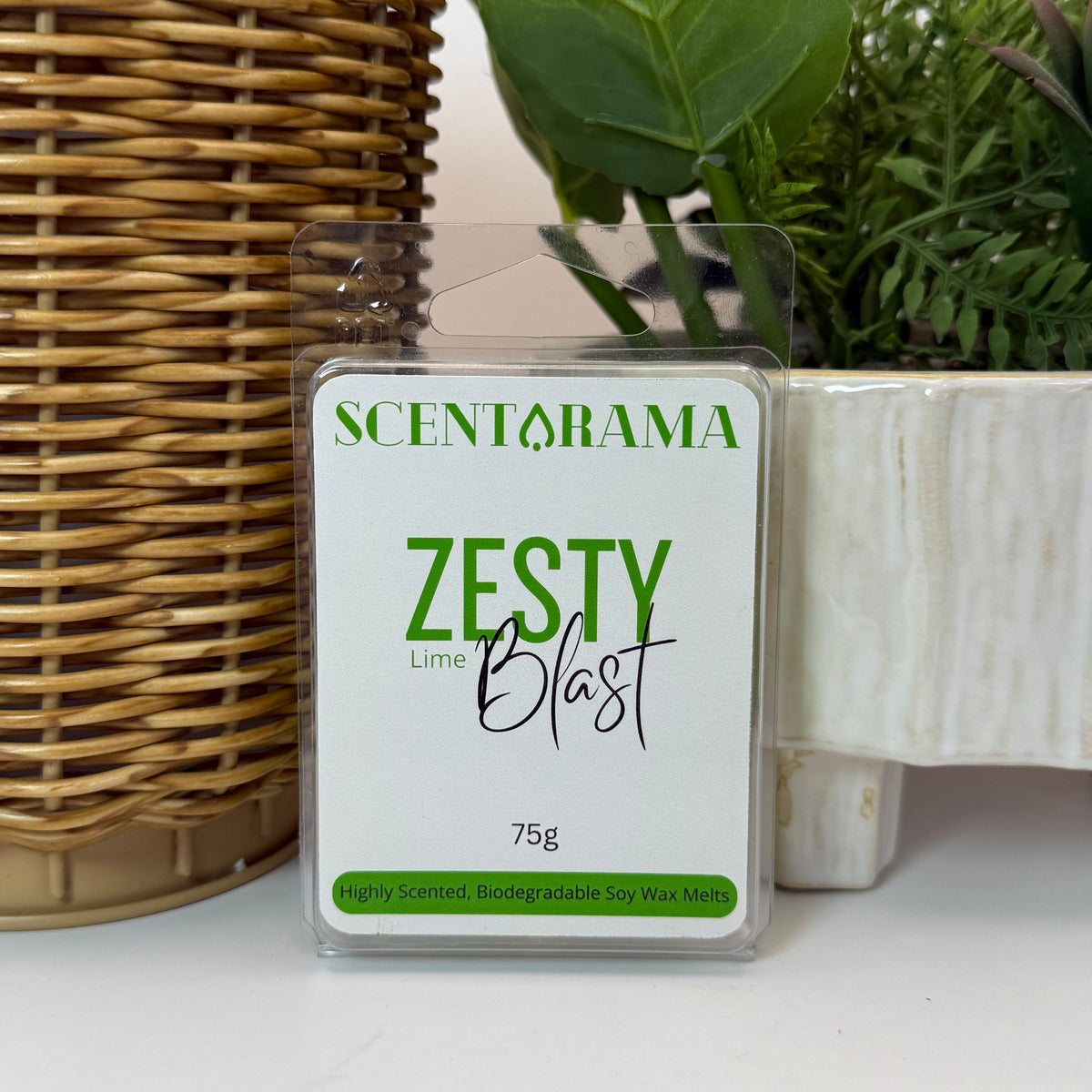 A 75g package of Scentarama Zesty Blast Lime soy wax melts, displayed on a white surface with a wicker basket and potted plants in the background.